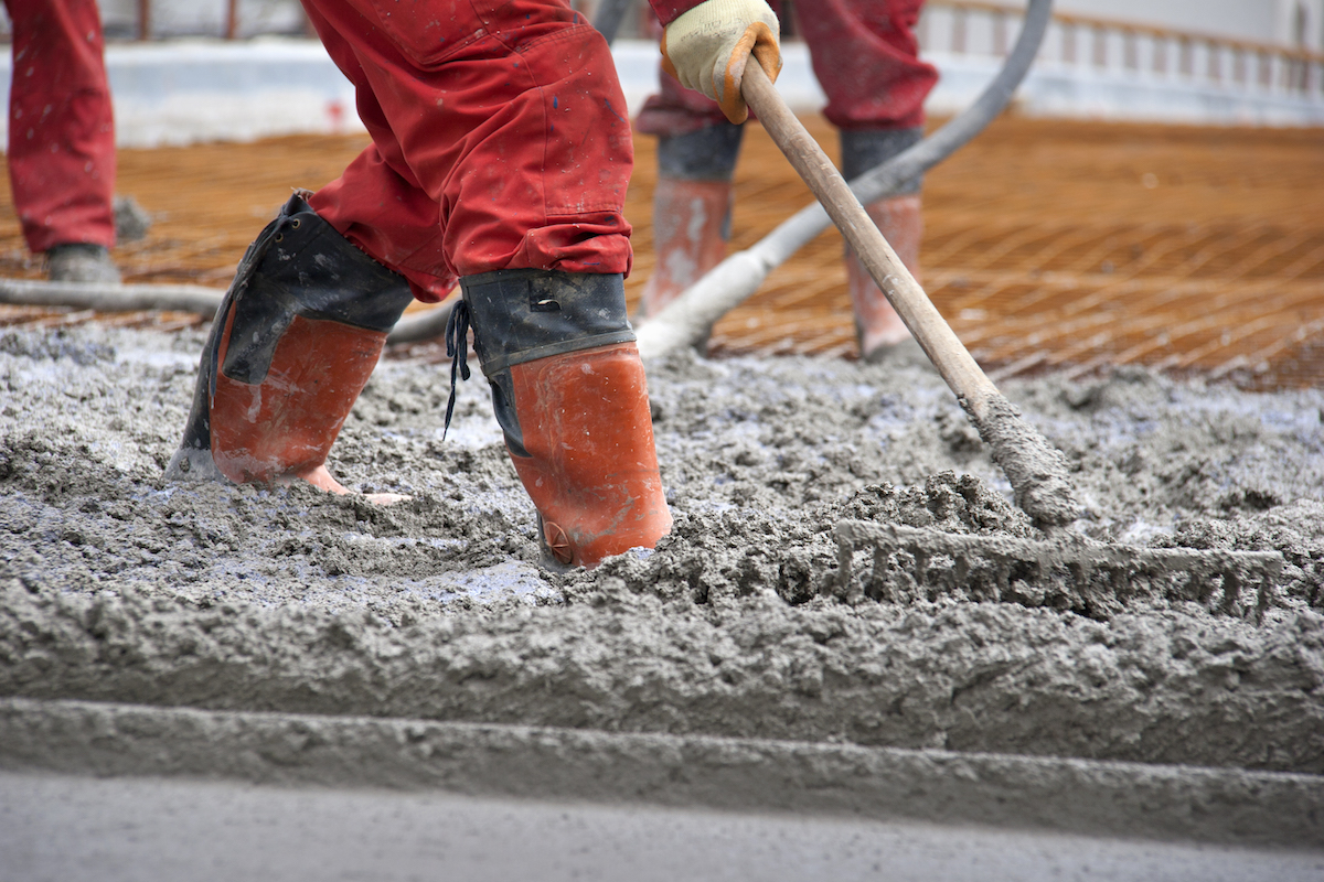 Workers in red boots with rake leveled the concrete